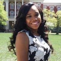 Picture of Deidra Bibbs smiling in front of a field and a brick building