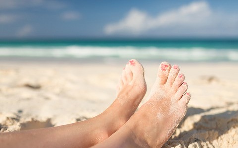 Bare feet on a sandy beach with painted toenails. 