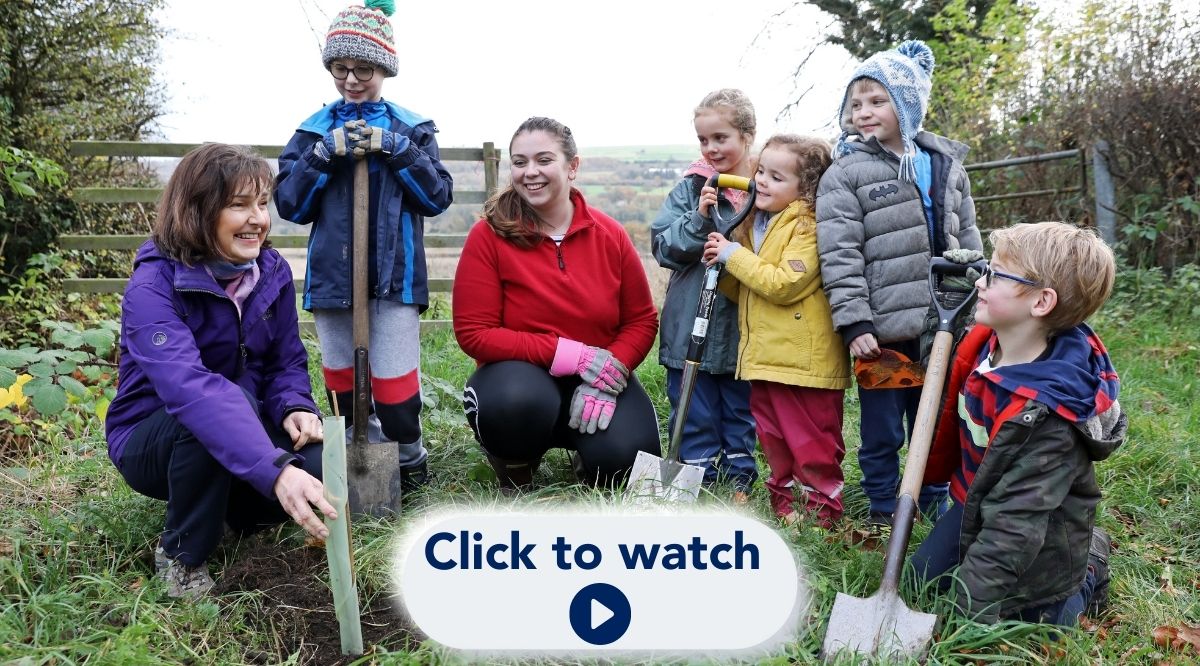 Tree planting group members teaching children how to plant tree saplings with text 'click to watch' overlayed