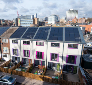 A photo of some modern insulated houses with solar panels in front of a city skyline