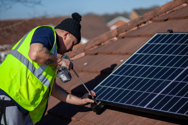 A man fitting solar panels to the roof of a building