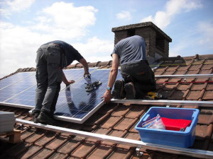 A photo of two workers installing solar panels on a rooftop