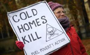 A woman wearing warm clothes holding a placard saying 'Cold Homes Kill - Fuel Poverty Action'