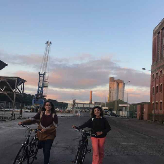 Photo of two women with bicycles and a city skyline backdrop