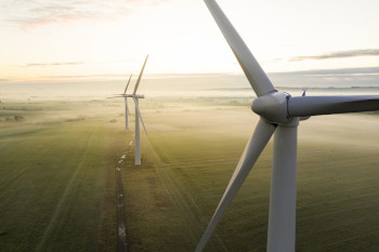 A photo of three wind turbines over fields