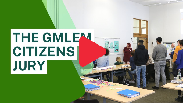 A screenshot from the video of a meeting room, with the text 'The GMLEM Citizens Jury', a play button is overlayed