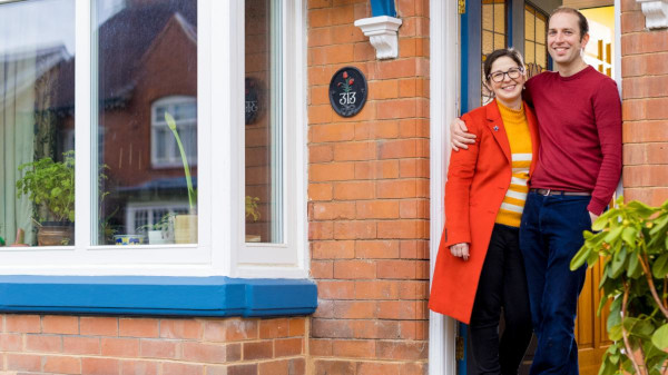 A man and a woman standing outside of their Victorian home