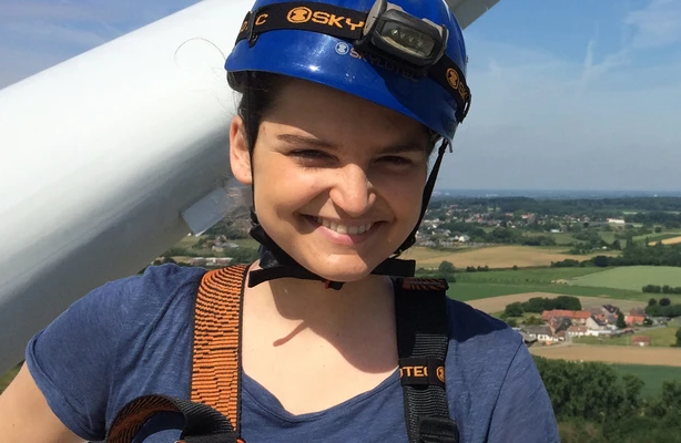 Photo of Ine Swennan at the top of a wind turbine wearing a helmet and harness