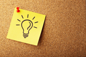A photo of a cork board with a post-it note with a picture of a lightbulb pinned on it.