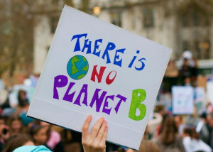A photo of a hand holding a colourful hand-drawn sign saying “There is No Planet B“