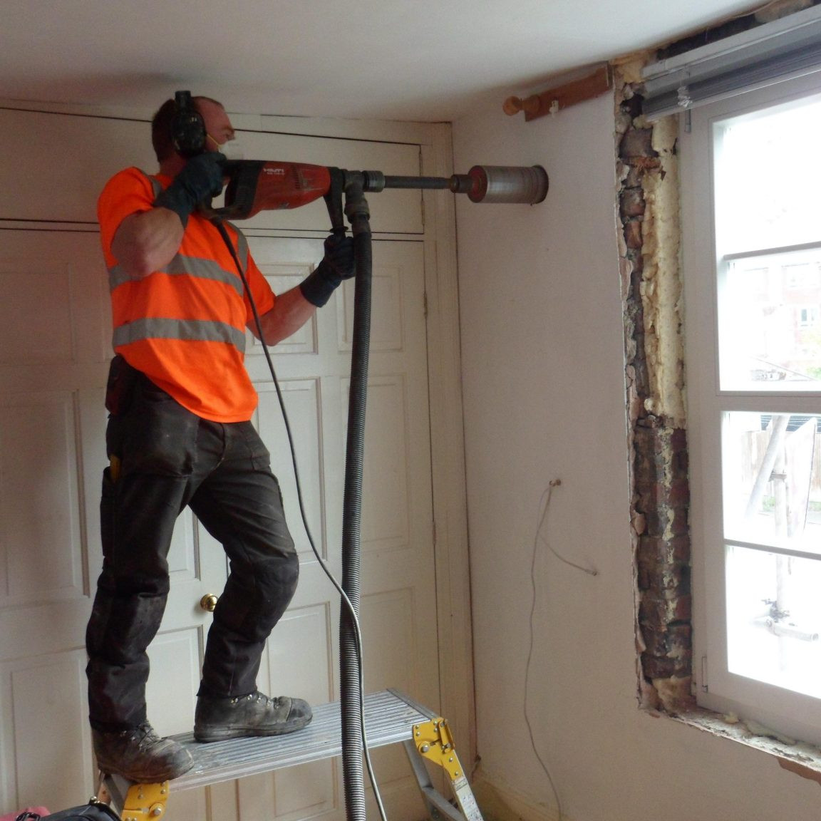 Photo of a builder drilling a hole in a wall to install ventilation
