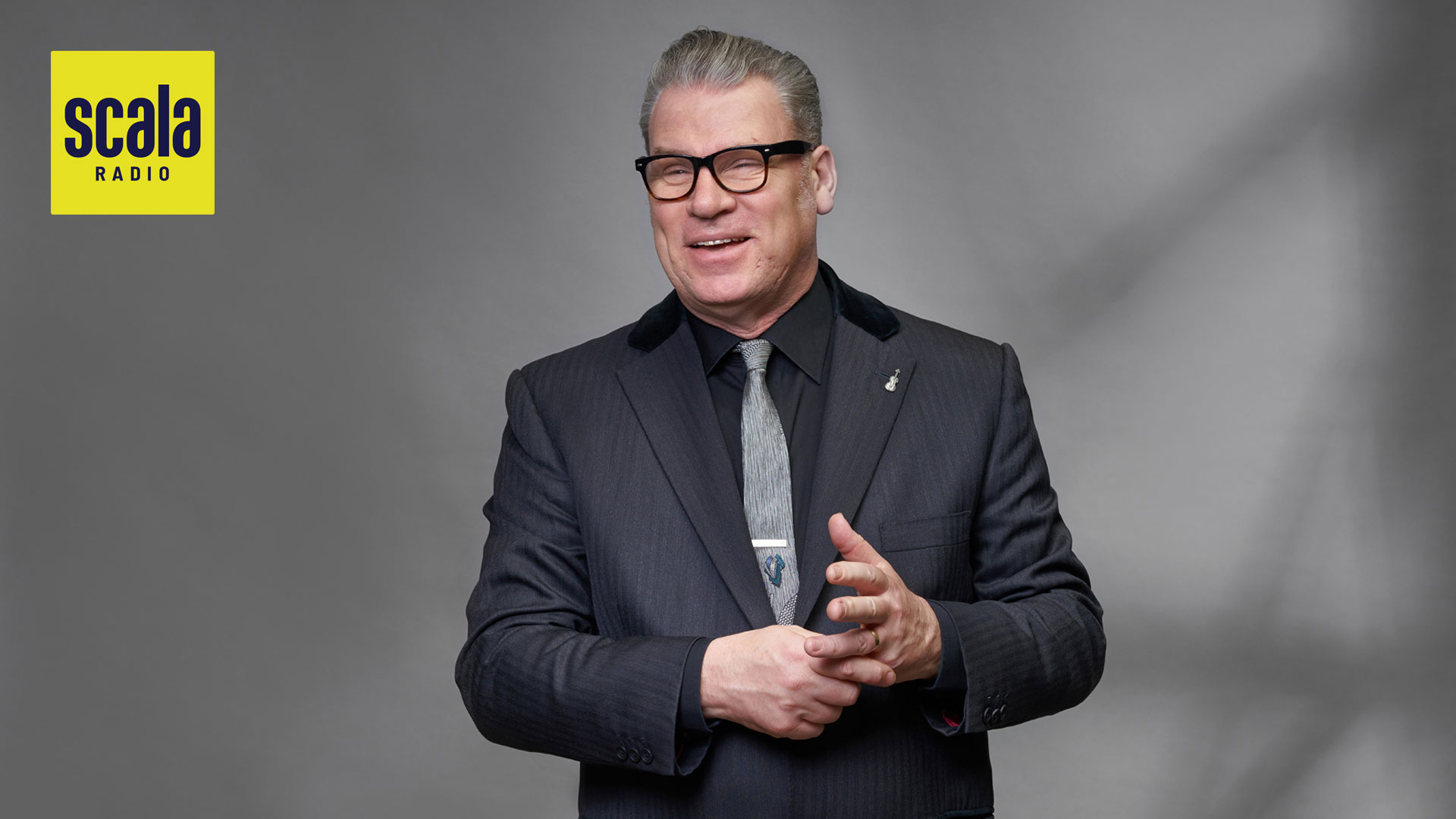 middle aged man in charcoal suit laughing and holding his hand