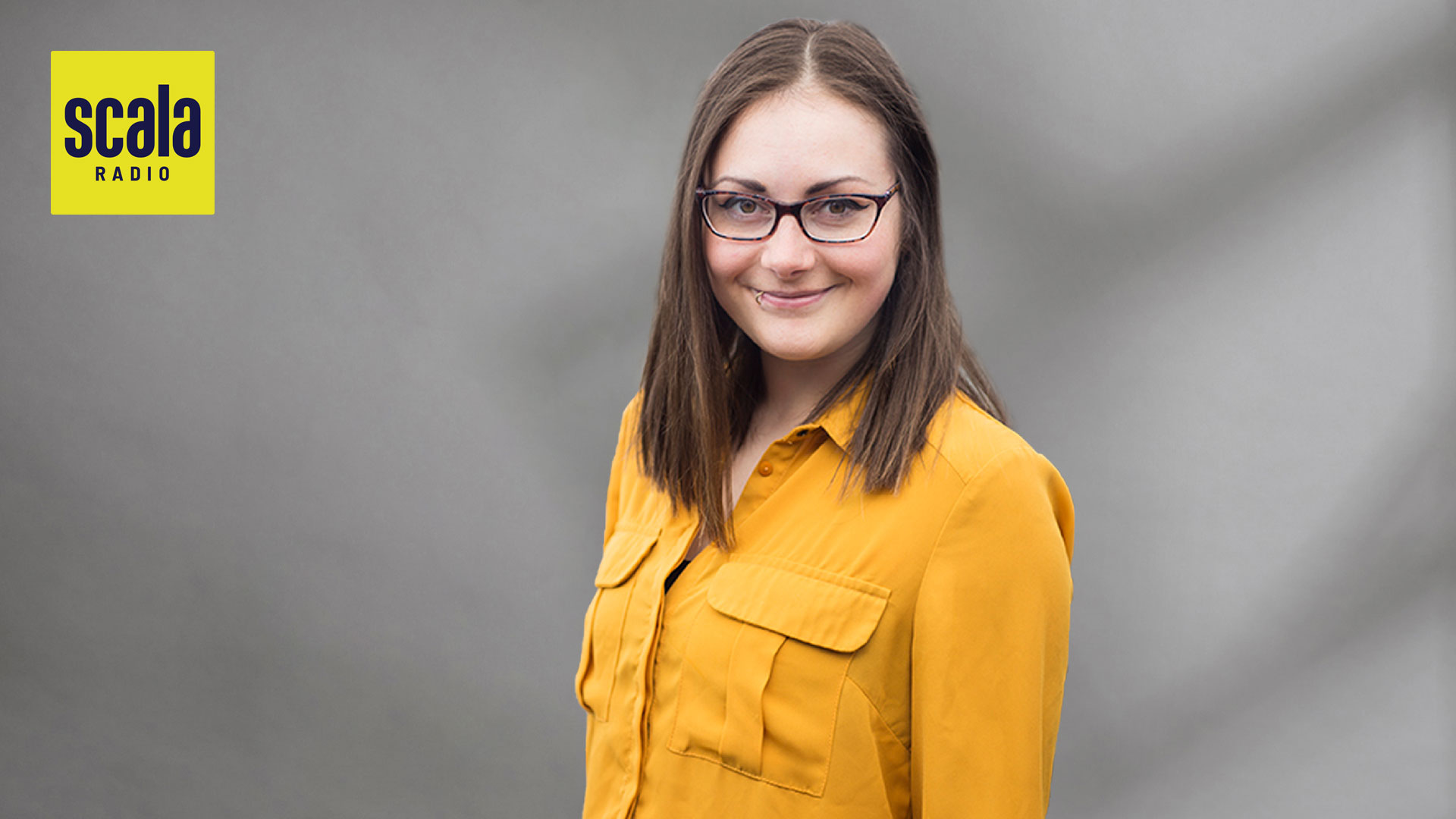 smiling woman in yellow shirt infront of grey background