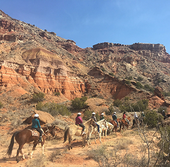 A group of people take a tour of Palo Duro Canyon on horseback.