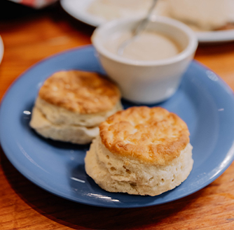 A blue plate of two biscuits with a cup of gravy on the side.